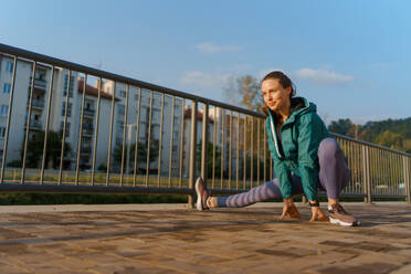 Junge Läuferin, die sich vor ihrem morgendlichen Lauf in der Stadt die Beine dehnt. Fitness-Mädchen in Sportkleidung, die sich auf das Abendtraining vorbereitet. Outdoor-Workout-Konzept. - HPIF35116