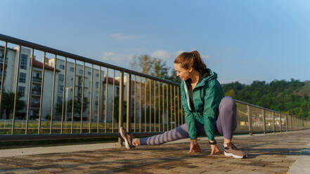 Junge Läuferin, die sich vor ihrem morgendlichen Lauf in der Stadt die Beine dehnt. Fitness-Mädchen in Sportkleidung, die sich auf das Abendtraining vorbereitet. Outdoor-Workout-Konzept. - HPIF35117