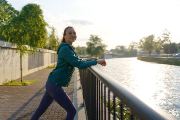 Side view of young female runner stretching before her early morning run. Fitness girl in sportswear preparing for evening exercise. Deep breathing exercises before workout. - HPIF35124