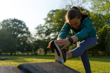 Porträt der jungen Fitness-Frau, die sich vor dem Training im Freien im Stadtpark dehnt. Gesunder Lebensstil Konzept. Kopieren Raum. - HPIF35131