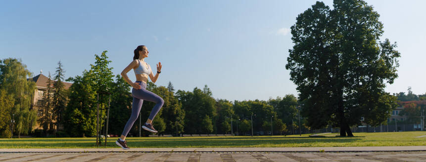 Seitenansicht einer sportlichen jungen Frau in Sportkleidung, die morgens in der Stadt läuft. Outdoor-Workout-Konzept. - HPIF35138