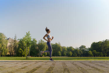 Seitenansicht einer sportlichen jungen Frau in Sportkleidung, die morgens in der Stadt läuft. Outdoor-Workout-Konzept. Banner mit Kopierbereich. - HPIF35139