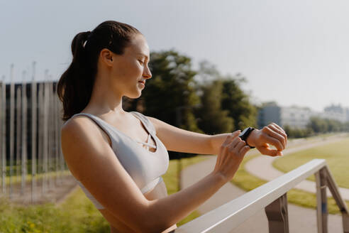 Seitenansicht einer sportlichen Frau, die nach dem Training ihre Leistung auf der Smartwatch überprüft. Die Frau benutzt die Smartwatch, um SMS zu senden und zu telefonieren. - HPIF35157