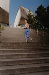 Porträt einer sportlichen Frau, die auf einer Betontreppe im Stadtpark läuft. Weibliche Athletin in Sportkleidung beim Treppentraining im Freien. Gesundes Lifestyle-Konzept. - HPIF35160