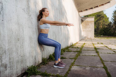 Portrait of young sporty woman in sportswear excercising outdoors. Fitness woman in front of concrete wall in the city. Healthy lifestyle concept. Street workout. - HPIF35169