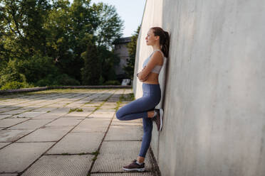 Seitenansicht einer jungen sportlichen Frau in Sportkleidung, die im Freien trainiert. Fitness-Frau vor einer Betonwand in der Stadt. Gesunder Lebensstil Konzept. Street Workout. - HPIF35170