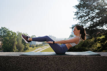 Seitenansicht einer jungen sportlichen Frau, die erhöhte Crunches auf einer Gymnastikmatte macht. Fitness-Frau, die im Freien Bauchmuskelübungen macht. Gesundes Lifestyle-Konzept, Street Workout. - HPIF35183