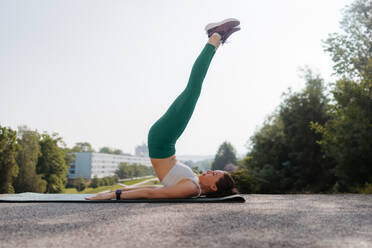 Side view of young sporty woman doing candlestick excercise on gym mat. Fitness woman doing abs exercises outdoors. Healty lifestyle concept, street workout. - HPIF35191