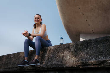 Junge Fitness-Frau in Sportkleidung, die sich nach dem Training in der Stadt ausruht. Schöne sportliche Frau genießt den Sonnenaufgang nach der Morgengymnastik. - HPIF35204
