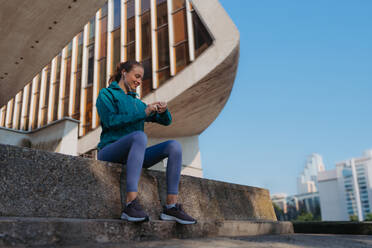 Seitenansicht einer sportlichen Frau, die nach dem Training ihre Leistung auf der Smartwatch überprüft. Die Frau benutzt die Smartwatch, um SMS zu senden und zu telefonieren. - HPIF35208