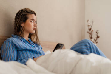 Junge Frau liegt auf ihrem Bett und scrollt auf ihrem Smartphone. - HPIF35232