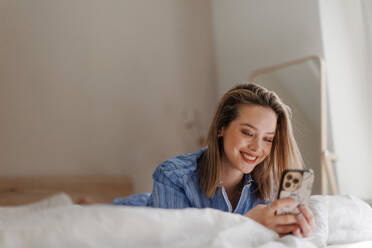 Junge Frau liegt auf ihrem Bett und scrollt auf ihrem Smartphone. - HPIF35240