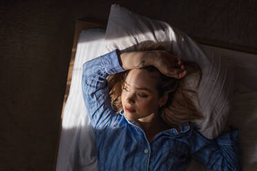 Blick von oben auf eine Frau, die in einem Bett liegt, die Morgensonne scheint auf ihr Gesicht. - HPIF35244
