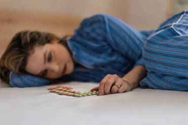 Junge Frau mit Depressionen, die im Bett liegt und auf die Pillen schaut. - HPIF35247