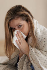 Porträt einer jungen kranken Frau, die in ihrem Schlafzimmer niest. - HPIF35249