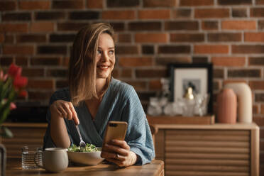 Young woman eating vegetable salad and scrolling her phone. - HPIF35255