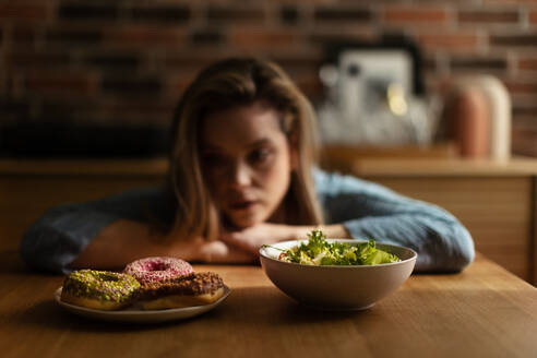 Junge Frau bei einer Diät, die sich zwischen einem Salat und Donuts entscheidet. - HPIF35256