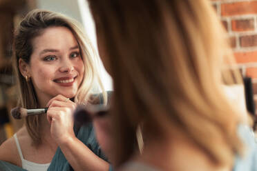 Junge Frau, die sich schminkt und in einen Spiegel schaut. - HPIF35260