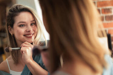 Young woman doing her make-up, looking in a mirror. - HPIF35260