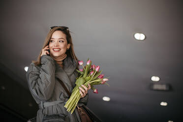 Junge Frau ruft in einer Stadt mit einem Tulpenstrauß an. - HPIF35265