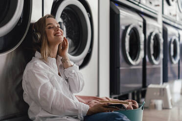 Junge Frau hört Musik und sitzt in einer Waschküche. - HPIF35268