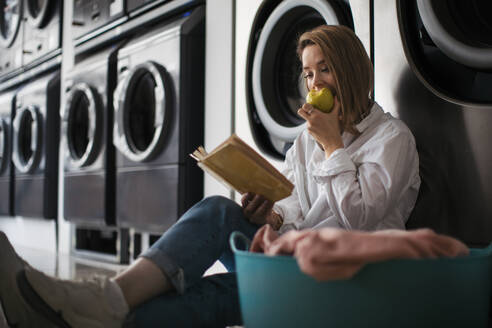 Junge Frau liest ein Buch und sitzt in einer Waschküche. - HPIF35269