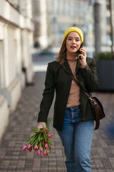 Junge Frau geht in einer Stadt mit Tulpen spazieren und ruft. - HPIF35273