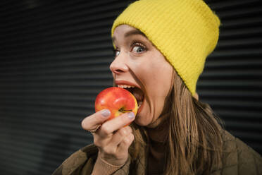 Porträt einer jungen, modischen Frau, die einen Apfel isst. - HPIF35281