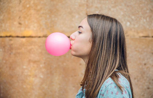 Closeup der schönen jungen Brünette Teenager-Mädchen bläst rosa Kaugummi über eine Steinmauer Hintergrund - ADSF50266