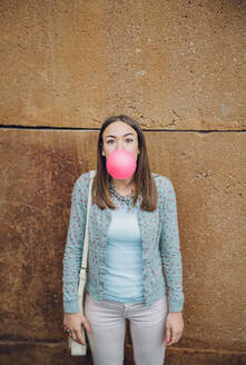 Porträt der schönen jungen Brünette Teenager-Mädchen bläst rosa Kaugummi über eine Steinmauer Hintergrund - ADSF50270