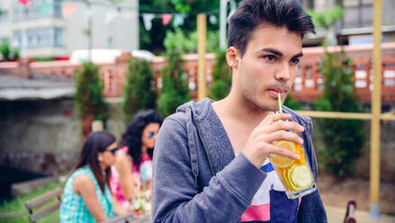Porträt eines jungen Mannes, der an einem Sommertag im Freien mit seinen Freunden, die im Hintergrund sitzen, einen Wassercocktail trinkt - ADSF50274