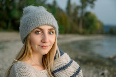 Side view of young woman in warm cozy sweater and hat, breathes clean air, looks at the sky with a smile and closed eyes, walks with pleasure in the autumn forest. people health content - ADSF50290