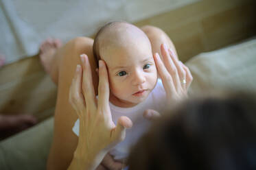 Von oben Handheld Schuss der Ernte Mutter berührt entzückende neugeborenes Baby und sprechen, während auf der Couch im Wohnzimmer zu Hause sitzen - ADSF50295