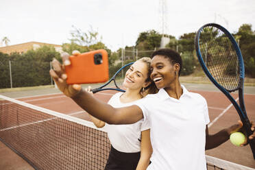 Porträt von zwei jungen schönen Frauen mit Tenniskleidung und Schlägern auf einem Tennisplatz, die bereit sind, ein Spiel zu spielen. - ADSF50301