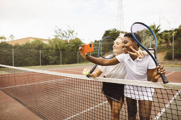 Porträt von zwei jungen schönen Frauen mit Tenniskleidung und Schlägern auf einem Tennisplatz, die bereit sind, ein Spiel zu spielen. - ADSF50302