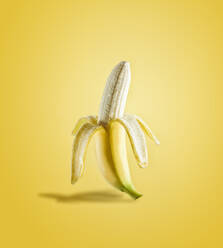 Half peeled banana in sunlight on yellow background. Delicious tropical fruit. Front view. - ADSF50336