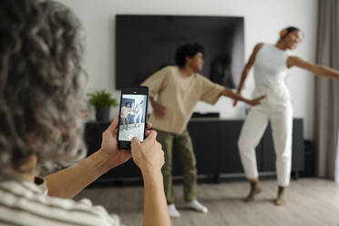 Mother using smart phone and filming video of her children dancing at home - DSHF01418