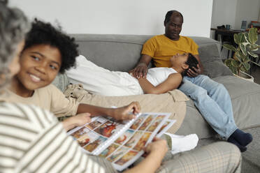 Son and mother reading comics and daughter resting on sofa with father - DSHF01419