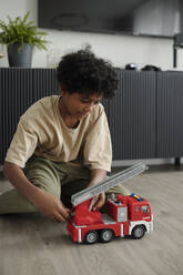 Boy playing with red fire truck toy at home - DSHF01432