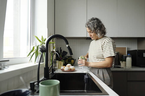 Mature woman pouring juice into glass at home - DSHF01437