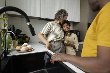 Mother kissing son standing by father in kitchen at home - DSHF01439