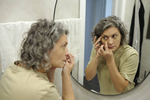 Woman applying under eye patches looking in mirror - DSHF01448