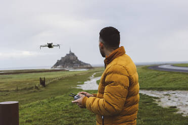 Man flying drone while standing by Saint Michel castle - JCCMF10966