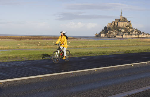 Woman riding bicycle on boardwalk by Saint Michel castle at weekend - JCCMF10971