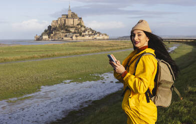 Woman with smart phone and backpack standing by Saint Michel castle - JCCMF10975