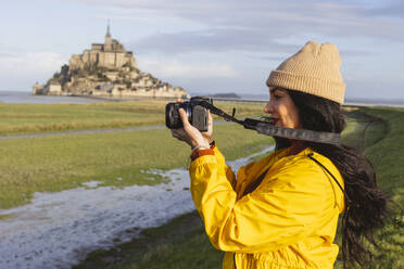 Woman photographing on camera by Saint Michel castle - JCCMF10977