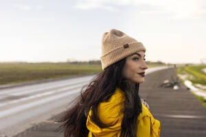 Contemplative woman with knit hat on street in front of sky - JCCMF10981