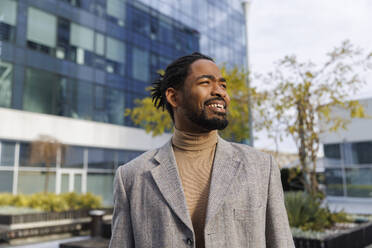 Smiling businessman wearing blazer and standing at office park - IKF01472