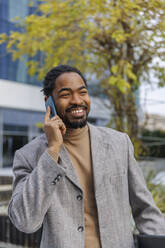 Happy businessman talking on smart phone at office park - IKF01479