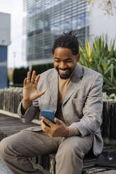 Smiling businessman waving on video call through smart phone - IKF01481